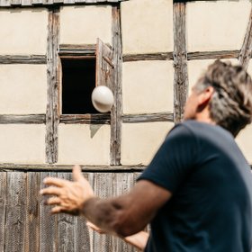 Ein Mann wirft einen Ball vor einem schönen Fachwerkhaus. Neue Höfe schafft regionale Werte neu.