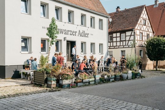 Neue Höfe. Treffen einer Gruppe Menschen vor dem schwarzen Adler.