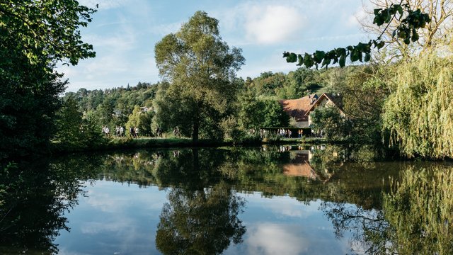 Landschaftsansicht: ein See von Bäumen umrandet, am hinteren Seerand sieht man ein Dorf. Menschen spazieren am Seeufer – Neuhof a. d. Zenn – fränkische Toskana und ländliche Idylle – Neue Höfe 