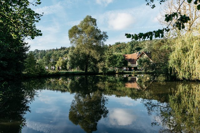 Landschaftsansicht: ein See von Bäumen umrandet, am hinteren Seerand sieht man ein Dorf. Menschen spazieren am Seeufer – Neuhof a. d. Zenn – fränkische Toskana und ländliche Idylle – Neue Höfe 