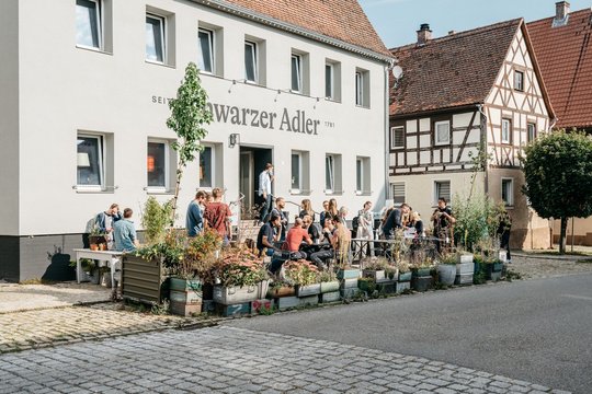 Neue Höfe. Treffen einer Gruppe Menschen vor dem schwarzen Adler.