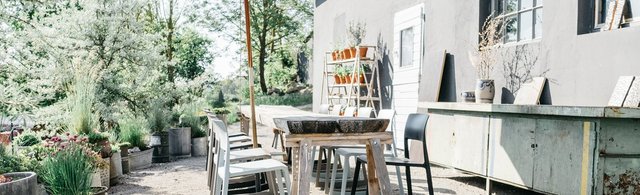 Großer Besprechungstisch im Freien, moderne und idyllische Außenterrasse des Wirtshaus am Hammerhof, Kies-Terrasse mit modernem Mobiliar, üppiger Begrünung, entspannte Atmosphäre, Neue Höfe 