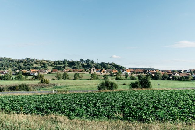 Neuhoff/Zenn, Panoramaaufnahme einer idyllischen Landschaft mit einem kleinem Ort mit Stadtmauer, viel Wiesen und Bäumen, Erlebnisort Neue Höfe 